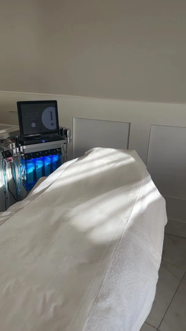 A made-up treatment bed beside the Hydrafacial machine